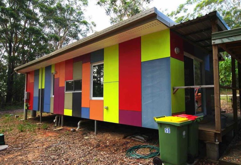 A wide shot of the 40-foot shipping container tiny house showing its sleek black exterior and large wooden deck on Russell Island