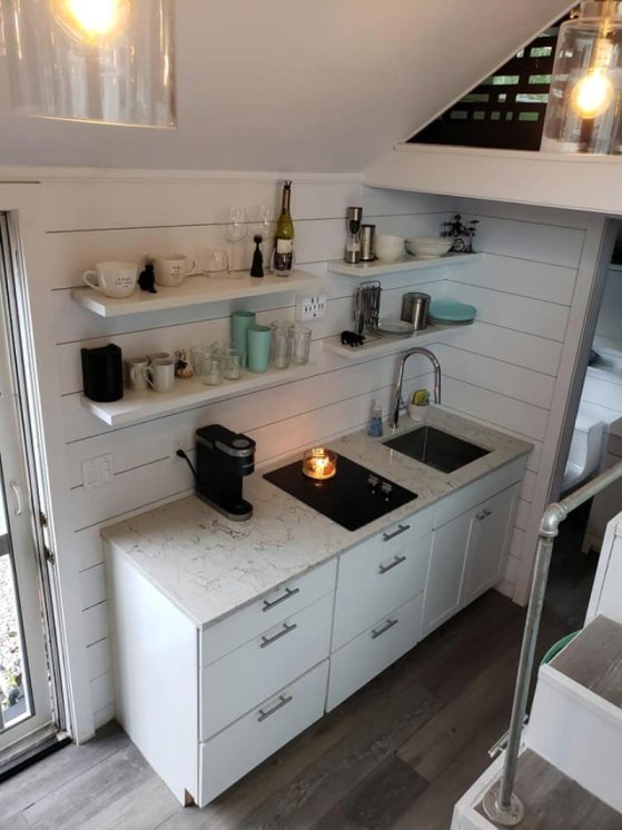 Interior of a tiny house kitchen with granite countertops, stainless-steel sink, and white open shelves.